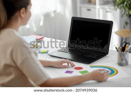 distant education, school and people concept - female elementary school teacher with laptop computer and picture of geometric shapes in different colors having online class at home