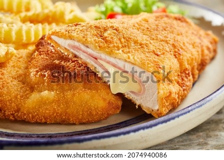 Closeup of delicious cordon bleu made of chicken and cheese served on plate with crinkle cut fries and vegetable salad prepared for lunch Royalty-Free Stock Photo #2074940086