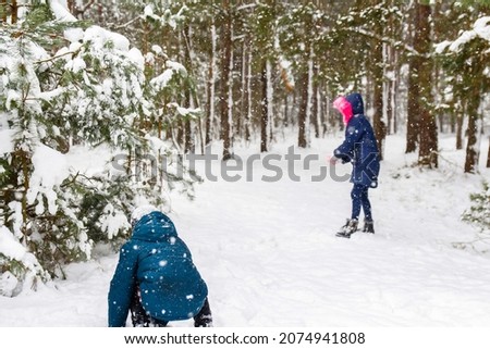 The boy sculpting a snowball with a girl. Funny children in Winter Park playing snowballs, actively spending time outdoors. Winter snowy woodland. Cold frost weather. Tween. Sibling. Rear view.