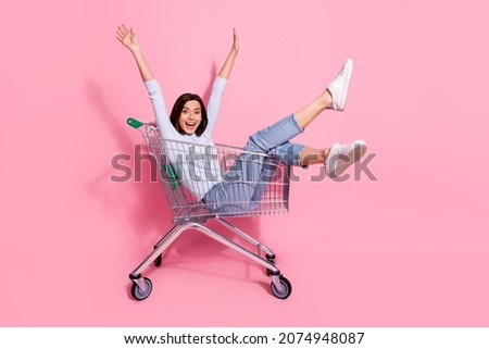 Photo of adorable funky young lady dressed white jumper smiling having fun shopping trolley isolated pink color background