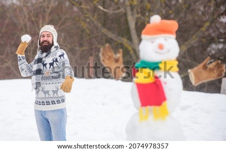 Leisure on fresh air. Snowman and cheerful bearded hipster knitted hat and warm gloves play with snow outdoors. Have fun winter day. Let it snow. Christmas holidays. Active lifestyle. Snow games