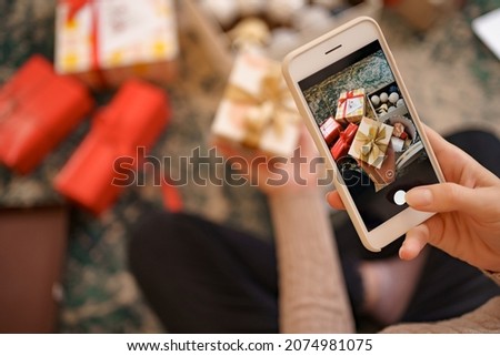 Flat lay of Woman s hands wrapping Christmas gift and taking pictures on the phone.