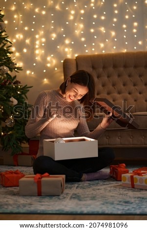 Pretty brunette woman opens an adorable present with lights in background