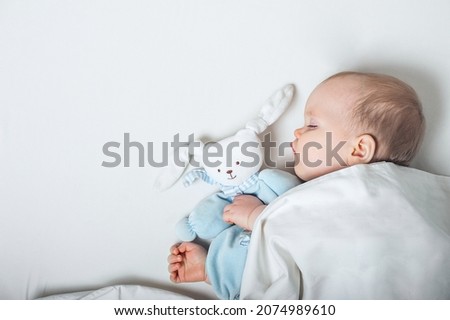 Baby with toy in hands sleeps on bed. Infant development concept, toddler restful sleep, teething, colic. Royalty-Free Stock Photo #2074989610