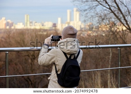 Girl in a coat taking pictures on smartphone camera of autumn city. Travel and holidays at fall and winter season