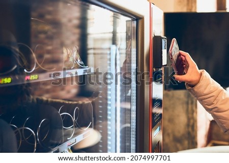 Woman paying for product at vending machine using contactless method of payment with mobile phone. Woman using new way of payments Royalty-Free Stock Photo #2074997701