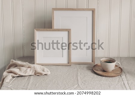 Portrait and square empty wooden frame mockups with cup of coffee. Beige linen table cloth. White beadboard wainscot wall paneling background. Scandinavian interior, home design. Art concept.