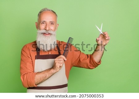 Portrait of attractive cheerful skilled well-groomed grey-haired man holding equipment isolated over green color background