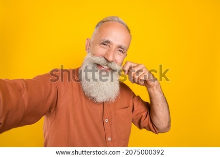 Photo of cheerful mature man make selfie hand touch mustache skin care lotion isolated over yellow color background