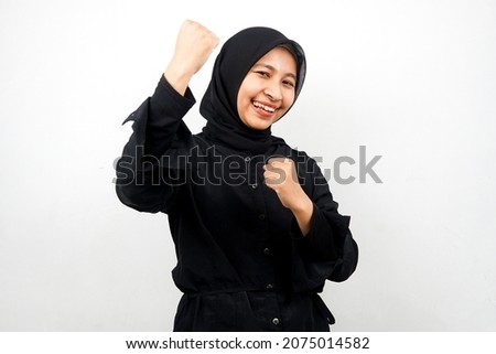 Beautiful young asian muslim woman smiling confident, enthusiastic and cheerful with hands clenched, sign of success, punching, fighting, not afraid, isolated on white background
