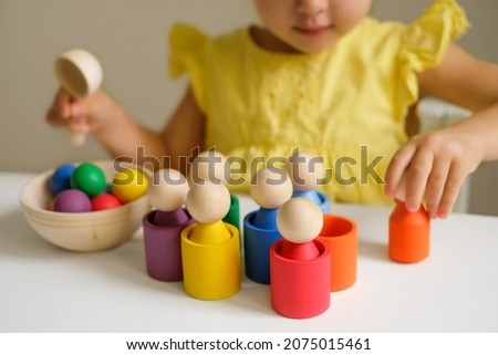 Wooden colored toy for learning colors and developing logic of preschoolers. A child plays at a table in the children's room with cups, balls and cylinders. Preschool education