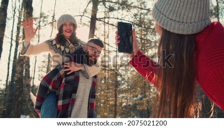Cheerful friends take photos having fun together at magnificent sunny snowy winter forest, Christmas holiday slow motion