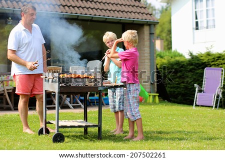 A father with sons, two twin teenage boys cooking meat on barbecue for summer family dinner at the backyard of the house Royalty-Free Stock Photo #207502261