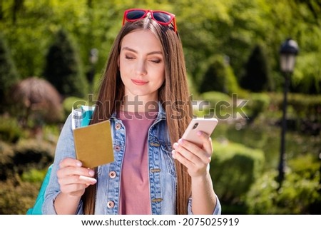 Photo of young attractive girl happy positive smile look read passport notebook use cellphone park summer nature