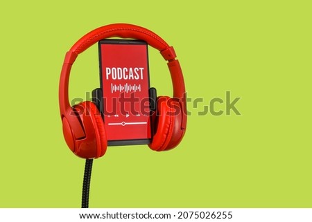 Modern headphones and mobile phone with podcast playlist on screen against color background Royalty-Free Stock Photo #2075026255