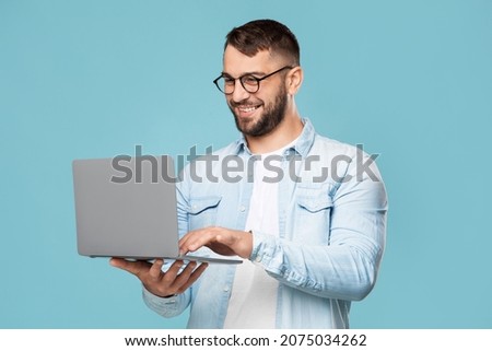 happy adult caucasian guy with glasses prints on the computer works remotely isolated on blue background.