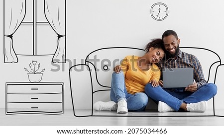 Cheerful young black couple look at laptop, sitting on floor in empty room with drawings on white wall background. Relocation, buy furniture for house or planning interior design using pc, panorama Royalty-Free Stock Photo #2075034466