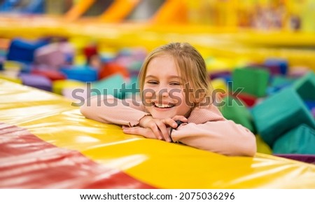 Pretty girl kid sitting in colorful cube trampoline at playground park and smiling. Beautiful female child happy during active entertaiments indoor Royalty-Free Stock Photo #2075036296