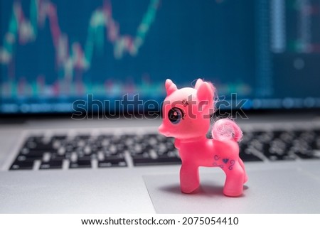 Unicorn toy on laptop on stock market graph background