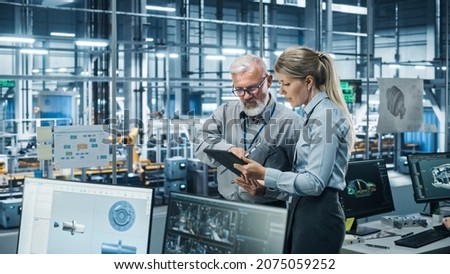 Car Factory Office: Manager Talks with Senior Engineer, Use Tablet Computer to Design Production Conveyor for Advanced Power Engines. Automated Robot Arm Assembly Line Manufacturing Vehicles Royalty-Free Stock Photo #2075059252