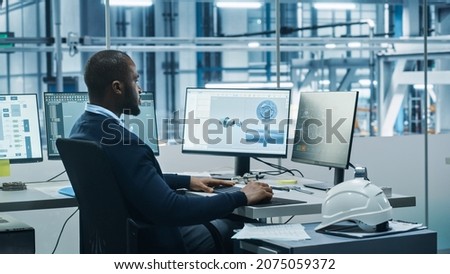 Car Factory Office: Black Engineer Working on Desktop Computer, Screens Show CAD Software with 3D Component, Monitoring of Automated Robot Arm Assembly Line Manufacturing High-Tech Electric Vehicles