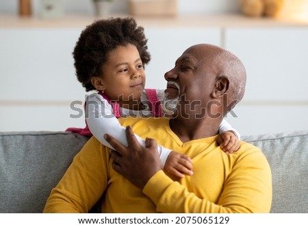 Cheerful little black girl play with older grandfather from back, hugging man at home interior. Family, people, relationships of generations during covid-19 lockdown. Positive active at living room Royalty-Free Stock Photo #2075065129