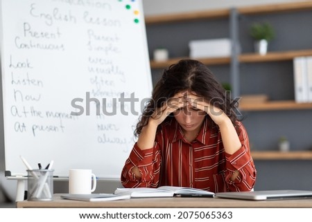 Portrait of tired concerned young lady feeling stress, tired of work upset about deadlines and troubles, suffering from headache, sitting at desk near whiteboard, thinking about problems issues Royalty-Free Stock Photo #2075065363