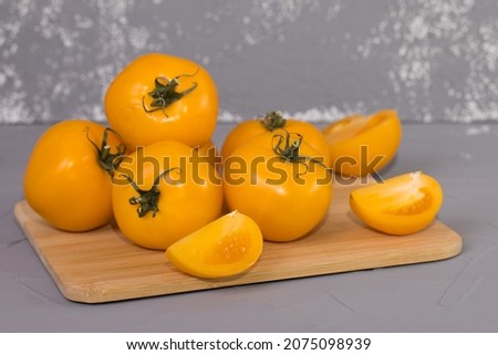 yellow tomatoes on brown wooden desk and grey background.