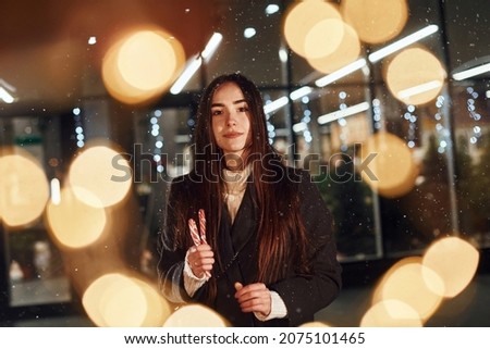 With candies in hands. Cheerful woman is outdoors at Christmas holidays time. Conception of new year.