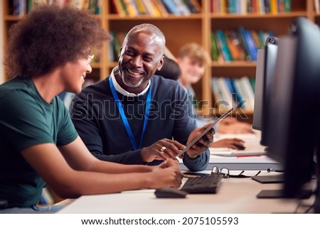 Male University Or College Student Working At Computer In Library Being Helped By Tutor Royalty-Free Stock Photo #2075105593