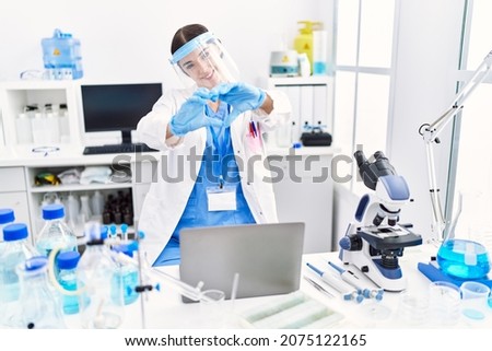 Young hispanic woman wearing scientist uniform smiling in love showing heart symbol and shape with hands. romantic concept. 