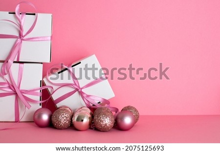 A small gift with a pink ribbon and pink christmass ball on pink background. White gifts with a pink bow. Christmas gifts. Gift for woman. Holiday background with gift, white satin 