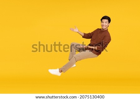 Happy cheerful young Asian man floating in the air isolated on yellow background, Presentation concept Royalty-Free Stock Photo #2075130400