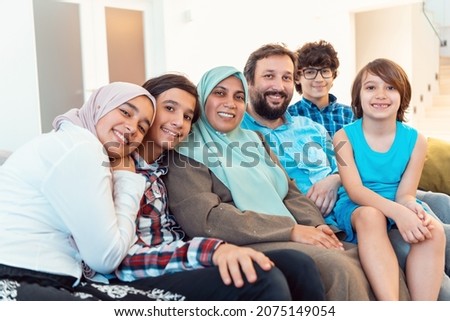 Portrait photo of an arab muslim family sitting on a couch in the living room of a large modern house. Selective focus  Royalty-Free Stock Photo #2075149054