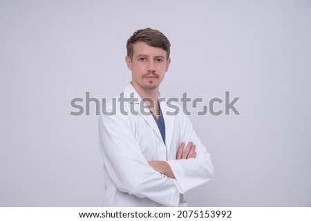 Portrait of young caucasian male medical doctor in white medical gown standing with crossed arms. Isolated on white. Looking at camera with copy space