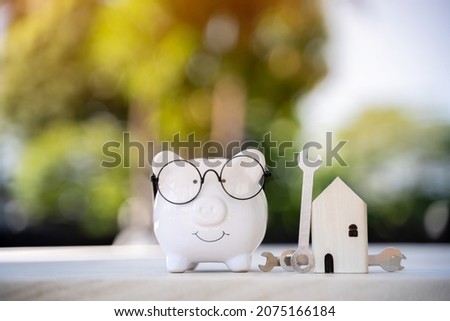 Piggy bank and home model with construction tools with repairing on the wood in the public park, Saving money and loan for renovation to real estate and house concept.