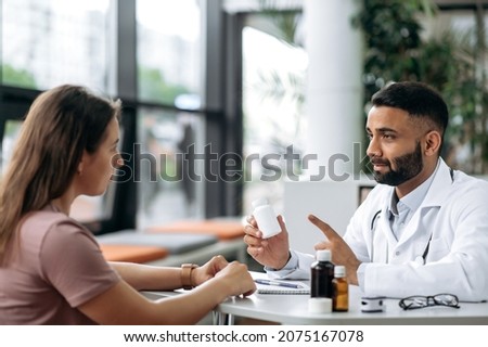 Consultation with a doctor in a clinic. Indian general medicine doctor in a medical uniform, advises the patient, prescribes treatment, listens to complaints, gives advice, shows medicines Royalty-Free Stock Photo #2075167078