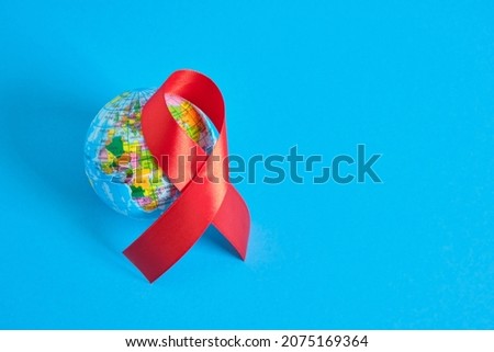 World AIDS day. The symbol of solidarity is a red ribbon nd toy globe ball blue background 1st december world aids day