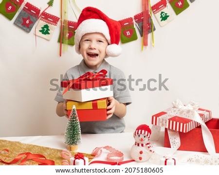 Funny joyful child boy in Santa red hat holding Christmas gift in hand over the festive background. New Year and Holidays concept.