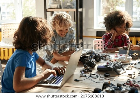 Multicultural happy diverse schoolchildren learning using gadgets and building robots on software robotics engineering class. Elementary school science classroom. STEM education concept. Cut image. Royalty-Free Stock Photo #2075188618
