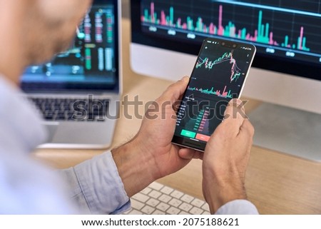 Crypto trader investor broker using smartphone app analyzing financial data stock market price on cell phone, checking online trading platform application, buying cryptocurrency, over shoulder view. Royalty-Free Stock Photo #2075188621