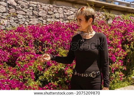 Portrait of an older woman walking down a path with violet flowers alongside. Concept of serenity and tranquility.