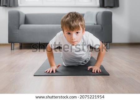 Boy-child doing classic push-ups at home in guest house on the floor on a sports mat
