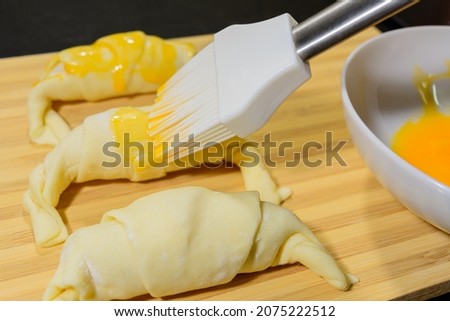 preparation of croissants, stuffed with ham and cheese and painted with egg yolk, on a wooden board, ready to bake