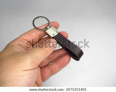 A man showing car keychain with a strap that has red stitches and carbon fiber texture