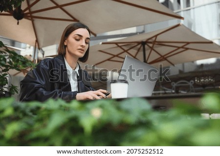 Beautiful concentrated woman, copywriter, freelancer working on laptop siting in summer terrace of a cafeteria. Distant remote online business concept
