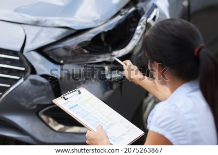 Insurance agent records damage to car after accident. Insurance indemnity in case of road accident concept Royalty-Free Stock Photo #2075263867