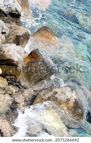 Colorful Volcanic Rock At A Shore line In The Mediterian Sea On Crete Island. Translucent Turquoise Waters Are Flowing Over the Stone. Agios Nikolaus, Crete, Greece. Abstract Water Photo.