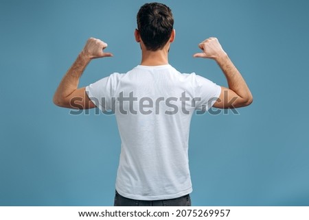 Back view of the caucasian man in T-shirt pointing at himself, while being proud and satisfied. Indoor studio shot isolated on blue background Royalty-Free Stock Photo #2075269957