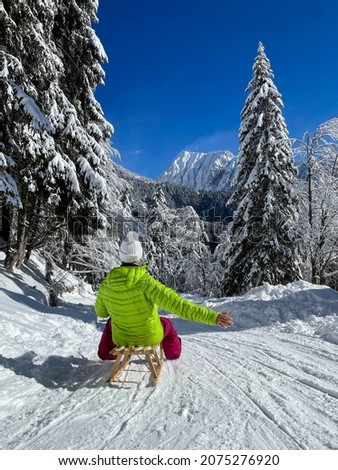 VERTICAL: Excited female tourist sledding in the Julian Alps outstretches her arm in joy as she speeds down a groomed ski resort slope. Unrecognizable woman is sleighing down a snowy forest trail.